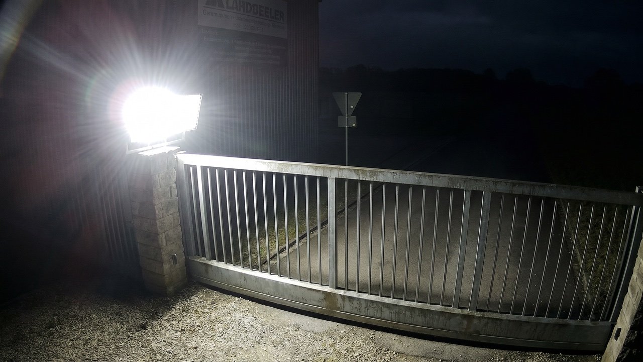 Tor bei Nacht: Ein Scheinwerfer überstrahlt den Vordergrund, der Weg dahinter liegt im Dunkeln